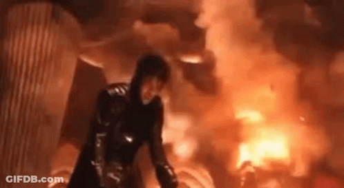 Woman In Black Suit Standing In Front Of Large Fire GIF