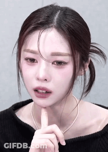 Woman In Black Sweater And Pearl Necklace Touching Chin GIF