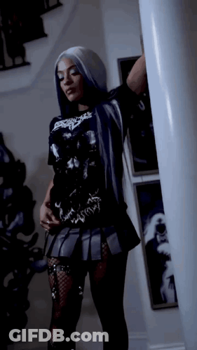 Woman In Black T-Shirt And Skirt Standing Next To Pillar GIF