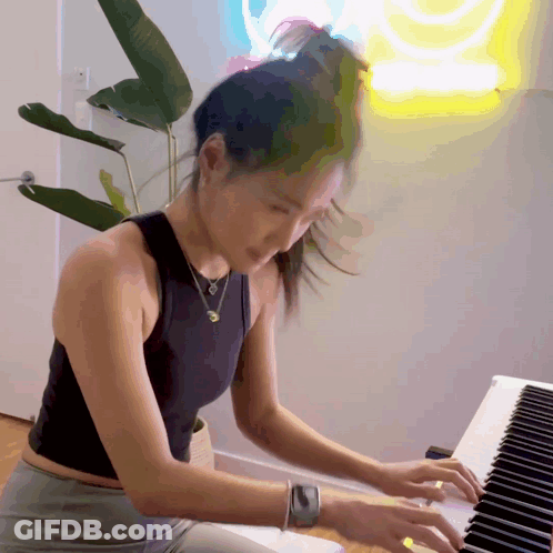 Woman In Black Tank Top Playing Piano In Front Of SpongeBob Neon Sign GIF