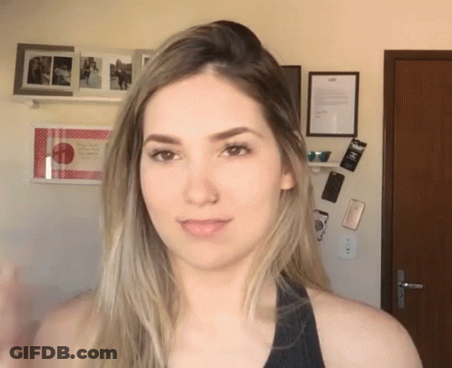 Woman In Black Tank Top Standing In Front Of Wall With Pictures And Sign Saying A GIF
