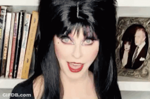 Woman In Black Wig In Front Of Bookshelf GIF