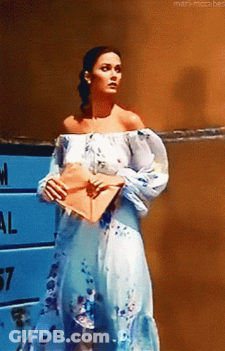 Woman In Blue And White Dress Holding Envelope In Front Of National Sign GIF