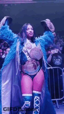 Woman In Blue Coat Holding Two Championship Belts GIF