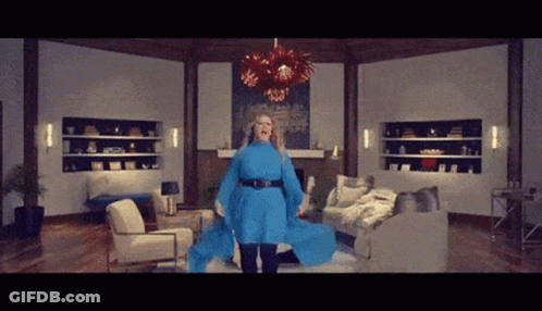 Woman In Blue Dress In Living Room With Couch And Chairs GIF