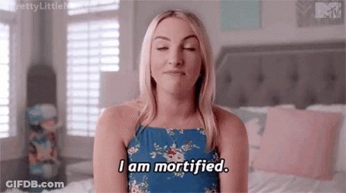 Woman In Blue Dress Sitting On Bed Eyes Closed Saying I Am Mortified GIF