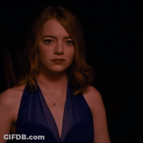 Woman In Blue Dress With Necklace Looking At Camera GIF