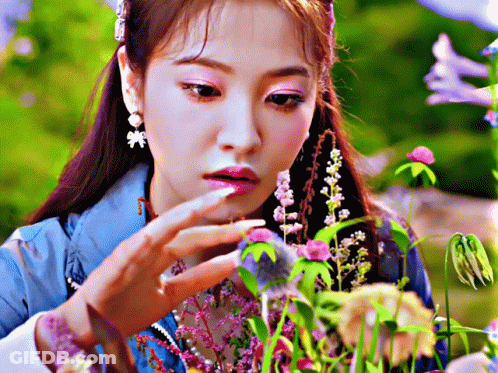 Woman In Blue Jacket Looking At Purple Flowers GIF
