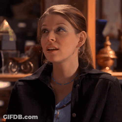 Woman In Blue Necklace And Black Jacket Looks To Side GIF