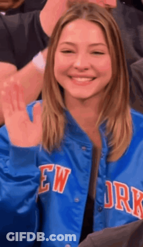 Woman In Blue New York Jacket Smiling And Waving GIF