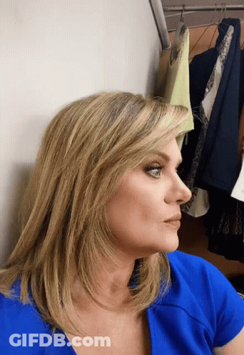 Woman In Blue Shirt Leaning Against Wall With Clothes GIF