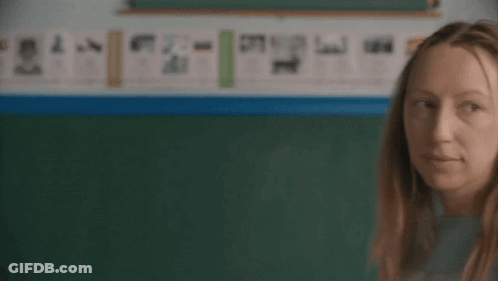 Woman In Blue Shirt Scratching Head In Front Of Blackboard GIF