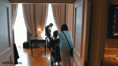 Woman In Blue Shirt Standing Next To Woman In Chair GIF