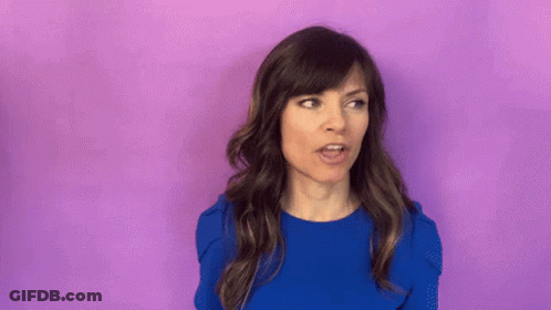 Woman In Blue Shirt Surprised In Front Of Purple Wall GIF