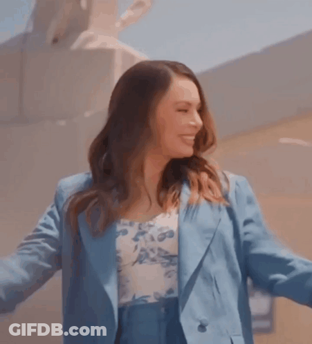 Woman In Blue Suit And Floral Top Smiling With Arms Outstretched GIF