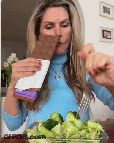 Woman In Blue Sweater Eating Broccoli And Milka Chocolate GIF