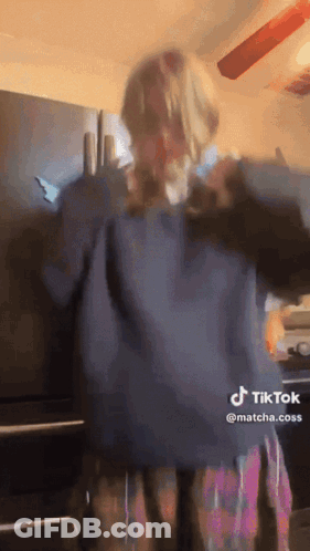Woman In Blue Sweater Plaid Skirt Dancing By Refrigerator GIF