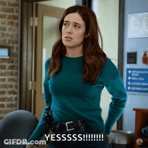 Woman In Blue Sweater Says Yesssss In Front Of Brick Wall GIF