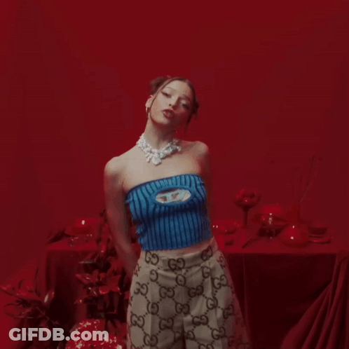 Woman In Blue Top And Gucci Skirt In Front Of Red Wall GIF