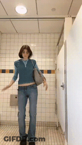 Woman In Blue Top And Jeans In Public Restroom GIF
