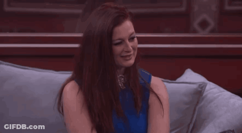 Woman In Blue Top Sitting On Couch With Hands On Chin GIF