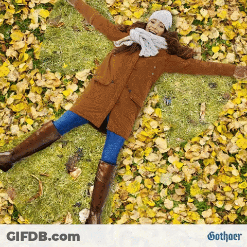 Woman In Brown Coat Laying On Yellow Leaves GIF