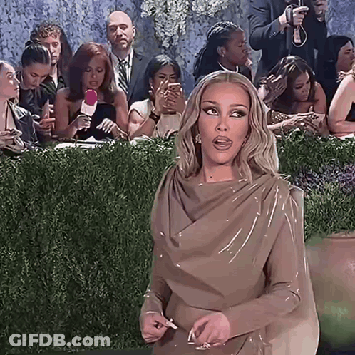 Woman In Brown Dress Standing Before Crowd GIF