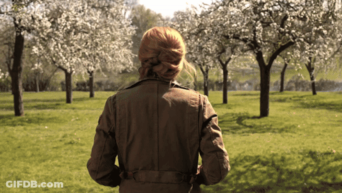 Woman In Brown Jacket Walking Through Blooming Park GIF