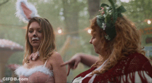 Woman In Bunny Ears Pointing At Woman In Flower Crown GIF