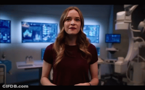 Woman In Burgundy Shirt Standing In Front Of Wall With Monitors GIF
