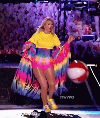 Woman In Colorful Outfit Holding Beach Ball On Stage GIF