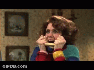 Woman In Colorful Sweater Holding Food In Mouth GIF