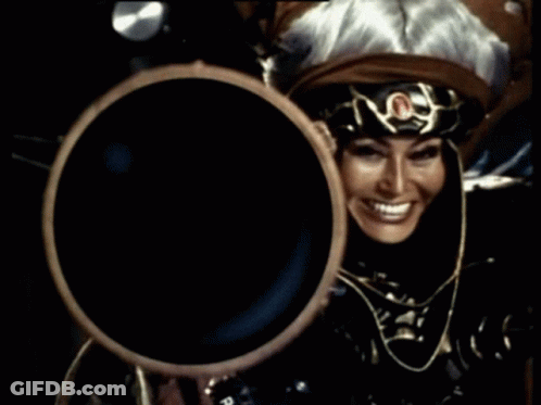 Woman In Costume Holding Large Object And Smiling GIF