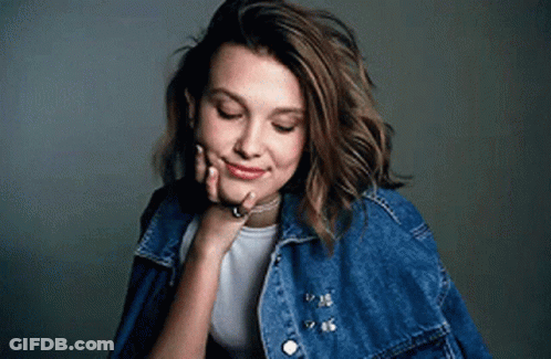 Woman In Denim Jacket And White Shirt With Hand On Face GIF