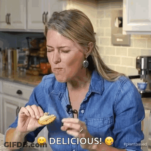 Woman In Denim Shirt Eating Cookie Saying Delicious GIF
