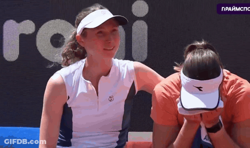 Woman In Diadora Hat Covering Face With Another Woman Looking On GIF