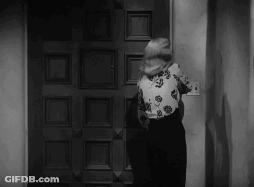 Woman In Floral Shirt Standing At Door In Black And White Photo GIF