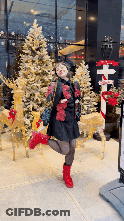 Woman In Front Of Christmas Tree With Sign Saying North Pole GIF