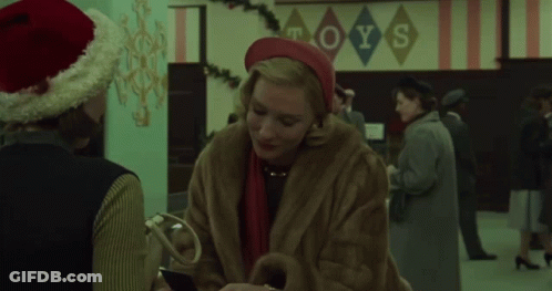 Woman In Fur Coat Talks To Man In Santa Hat Toys Sign GIF