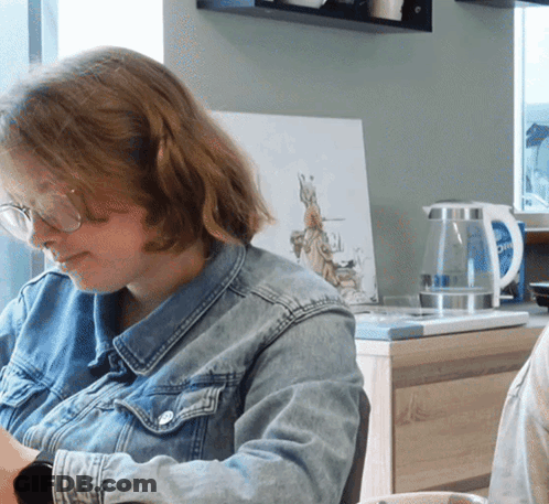 Woman In Glasses And Denim Jacket At Desk GIF