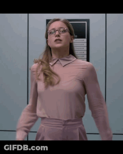 Woman In Glasses And Pink Shirt Standing Before Sign Saying A GIF