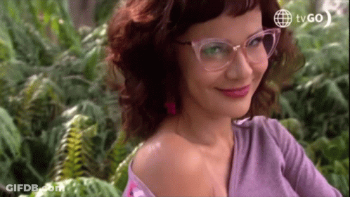Woman In Glasses And Purple Shirt Smiling In Front Of Ferns And TVGO Logo GIF