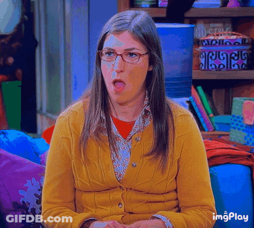 Woman In Glasses And Yellow Cardigan Sitting On Couch With Mouth Open GIF