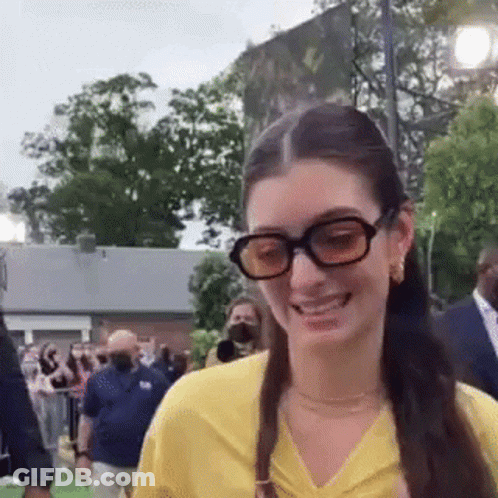 Woman In Glasses And Yellow Shirt Smiling At Crowd GIF