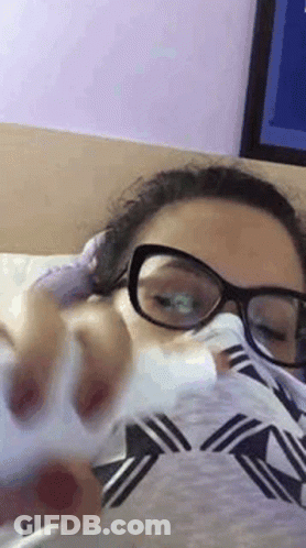 Woman In Glasses Laying On Bed With Tissue In Mouth GIF