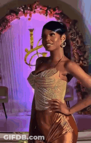 Woman In Gold Dress In Front Of Purple Wall With Flowers GIF