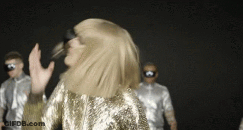 Woman In Gold Sequined Dress Dancing In Front Of Men In Silver Costumes GIF