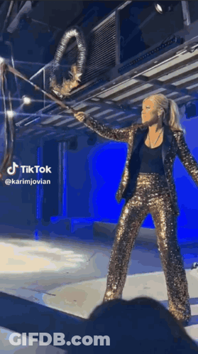 Woman In Gold Sequined Suit Holding Large Object GIF