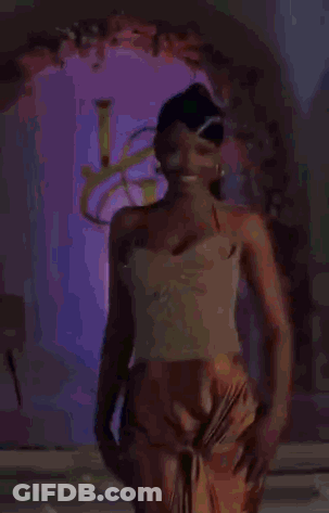 Woman In Gold Top And Orange Skirt In Front Of Purple Archway GIF