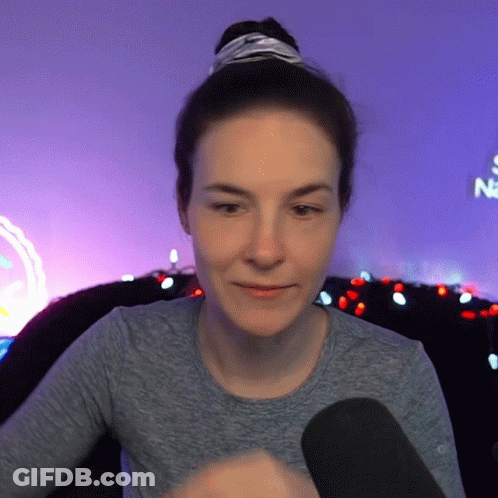 Woman In Gray Shirt Sitting In Front Of Neon Sign Saying Na GIF